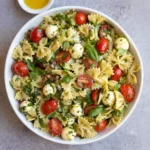 A modern glass bowl holding anti-inflammatory bow tie pasta salad on a bright white marble background.