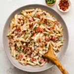 A modern glass bowl holding anti-inflammatory million dollar pasta salad on a bright white marble background.